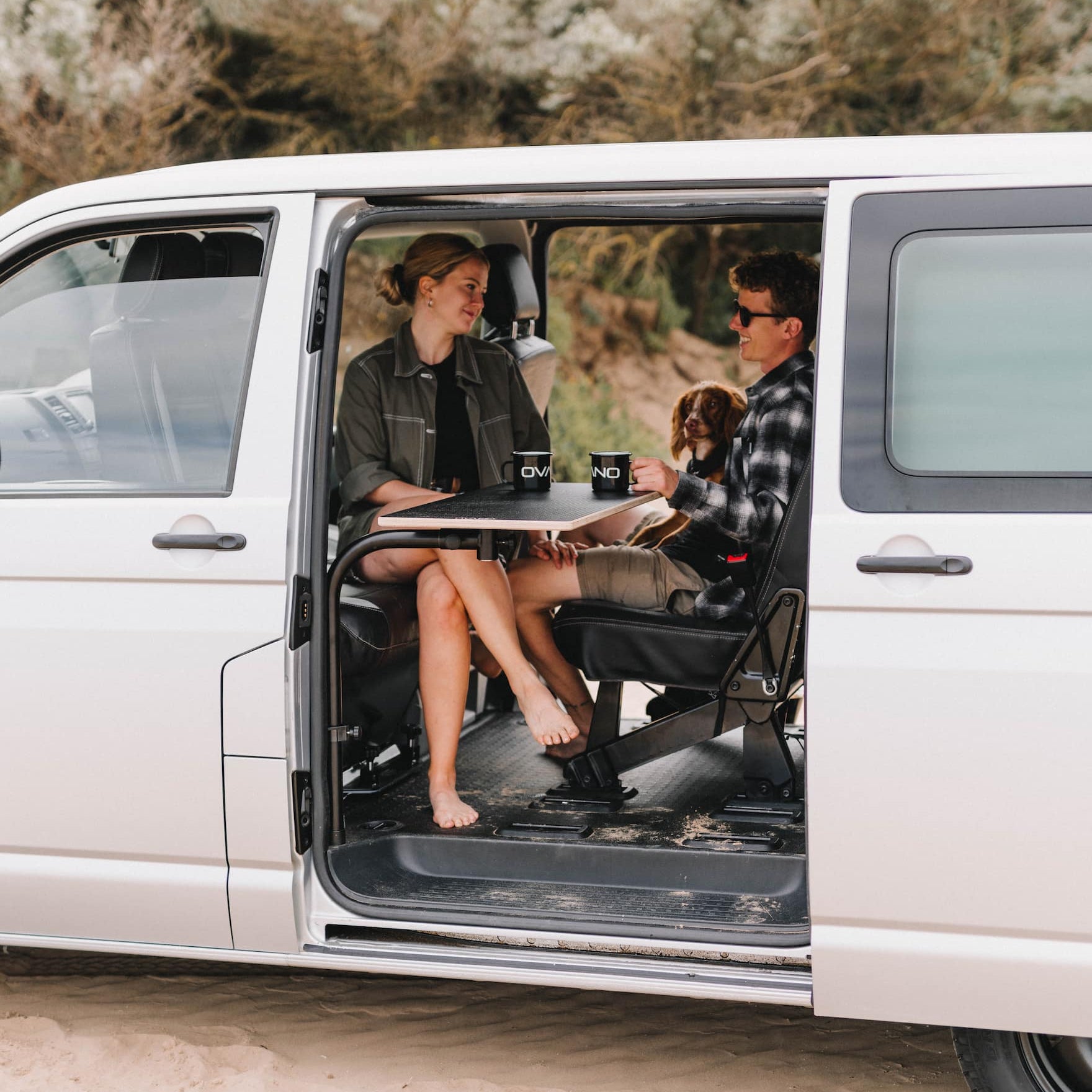 two people sat at an ovano table inside a van with the passenger seat swivelled