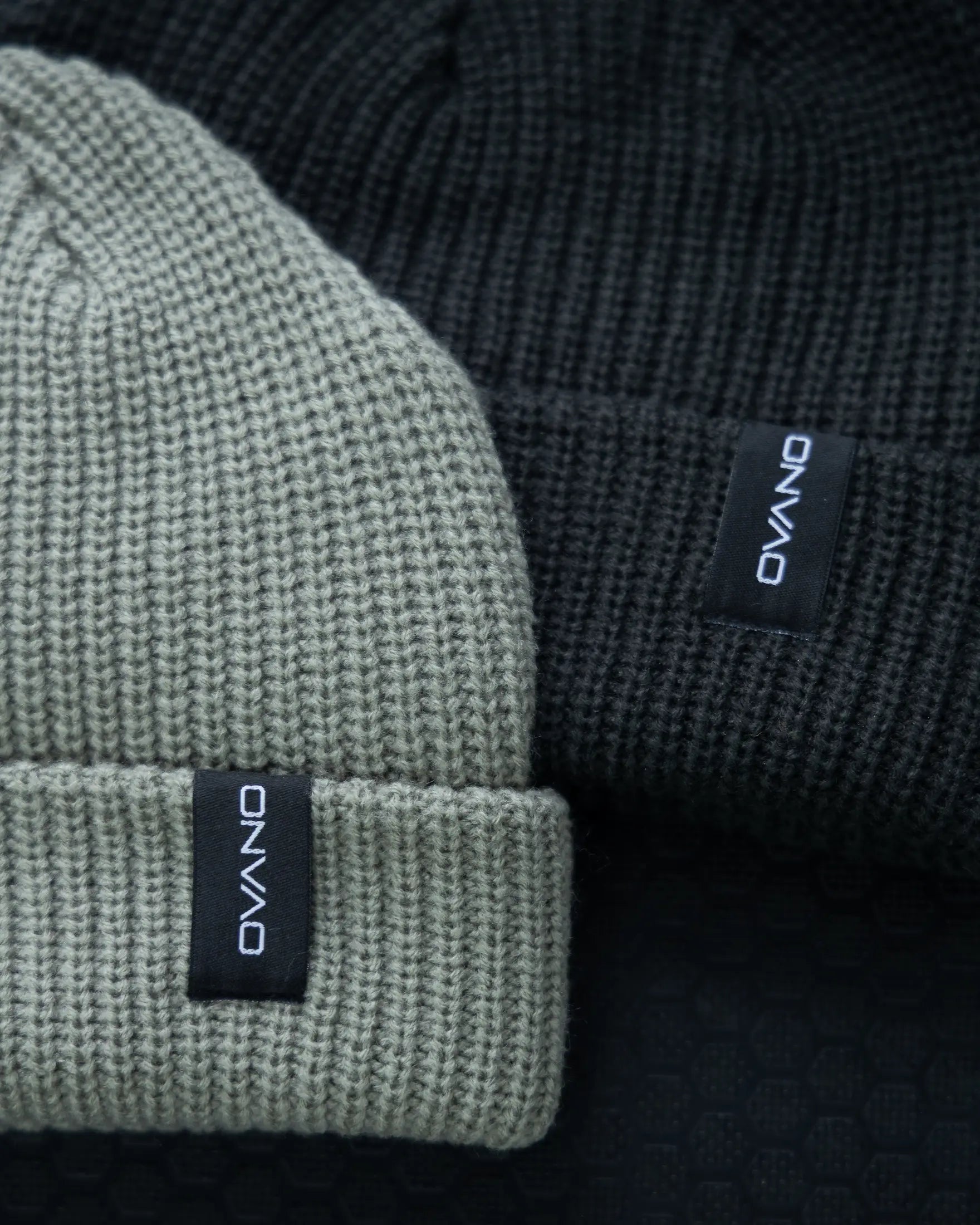 Two beanies, one green and one black, with a brand label on a dark background.