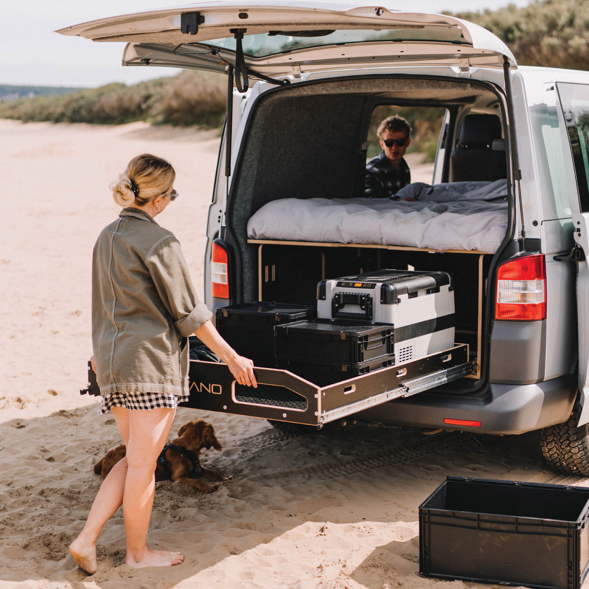 Person setting up a campsite in a vehicle with an open trunk on a beach.