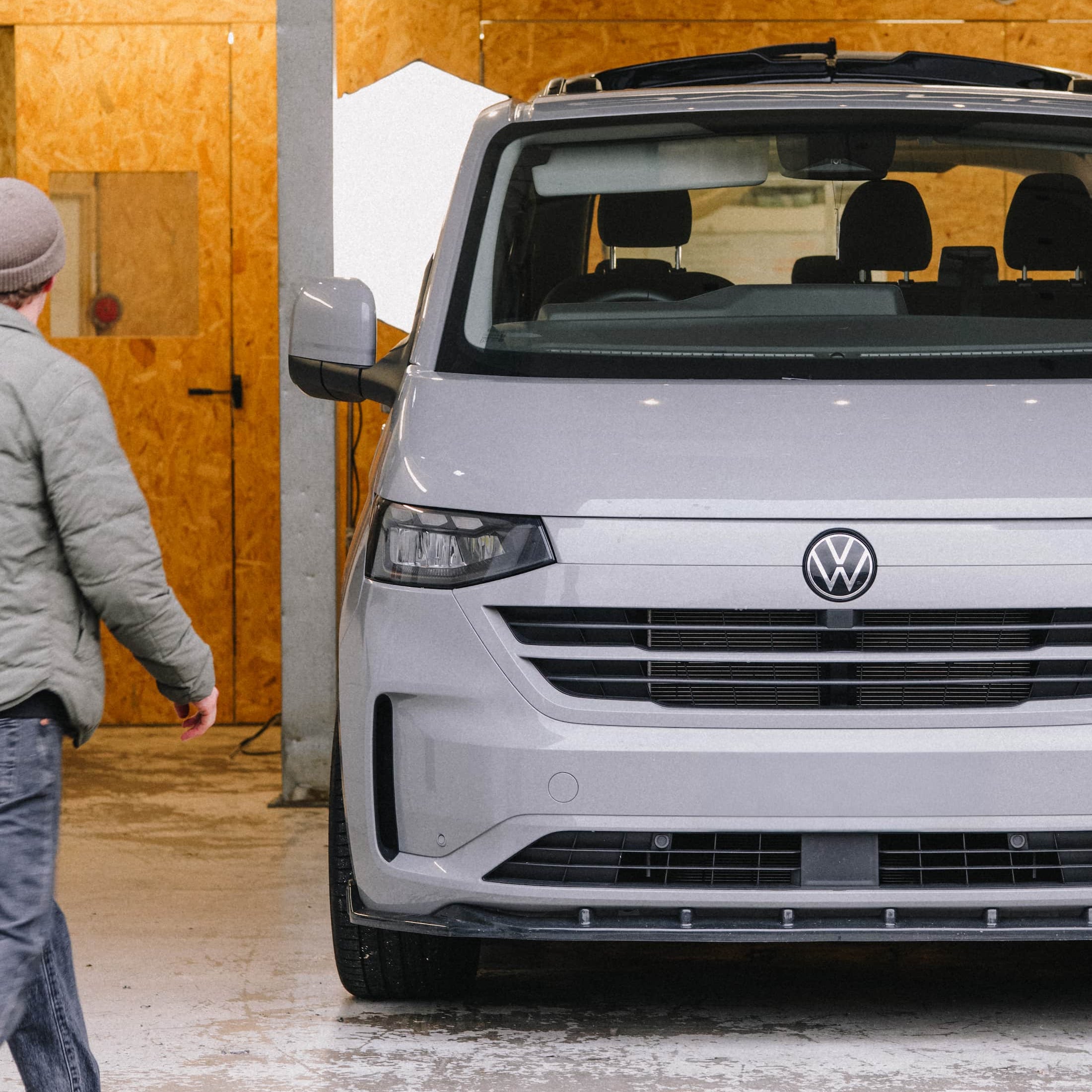 Person walking towards a Volkswagen Transporter T7 van in a workshop.