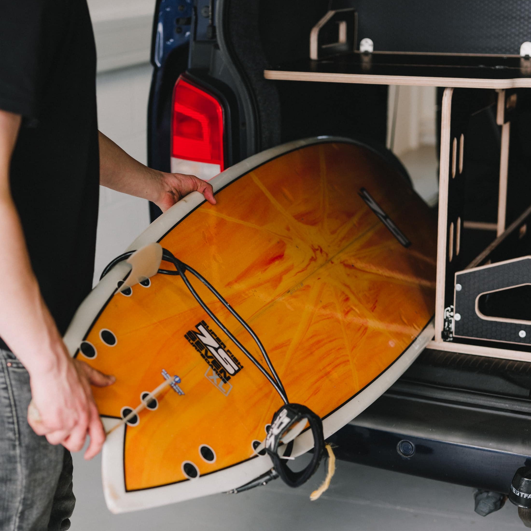 Person loading a surfboard into the rear of a VW Transporter